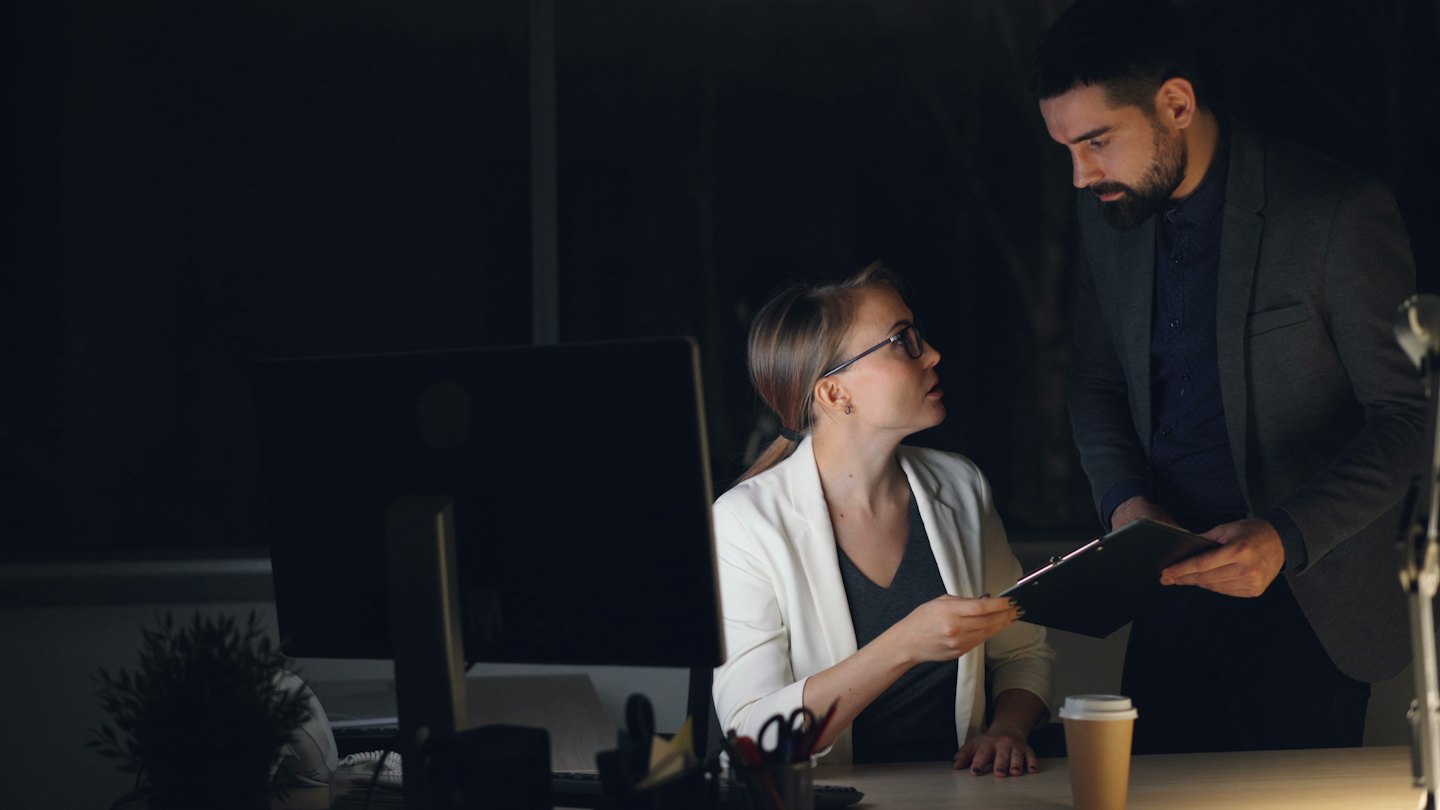 Business professionals discussing documents at a desk late at night.